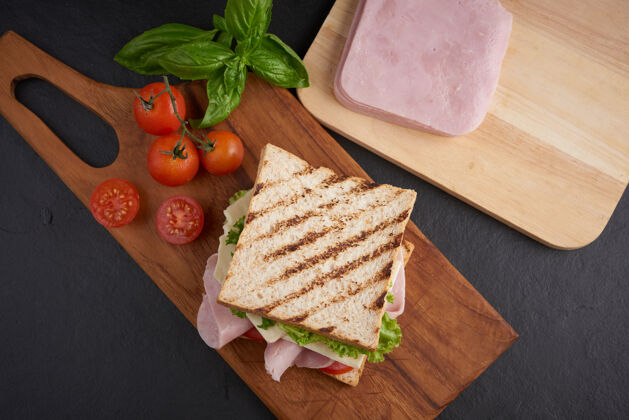 健康烤三明治配火腿 奶酪 西红柿和生菜 放在木制砧板上白色棕色火腿