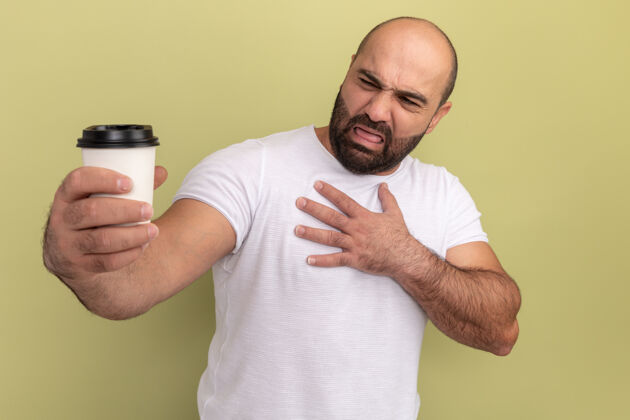 杯子一个留着胡子 穿着白色t恤的男人拿着咖啡杯 站在绿色的墙上 带着厌恶的表情看着咖啡杯厌恶咖啡胡须