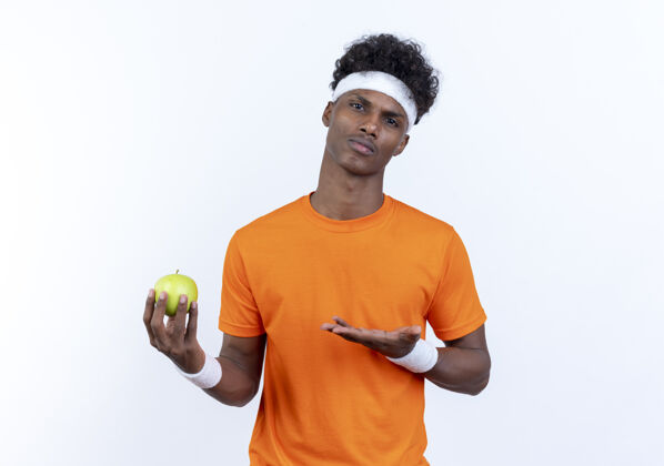 头带自信的美国黑人年轻人 戴着头带和腕带 手拿苹果指着他穿手腕带