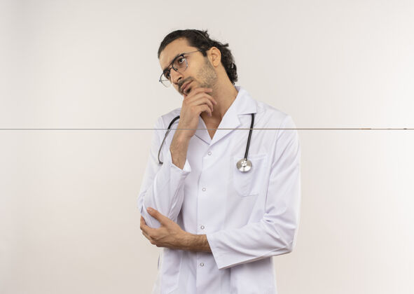 穿一边看一边想的年轻男医生戴着眼镜 穿着白色长袍 听诊器把手放在下巴上长袍男人眼镜