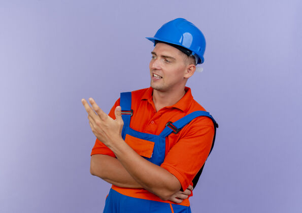 请看着身边高兴的年轻男建筑工人穿着制服 戴着安全帽点着手边男人点安全