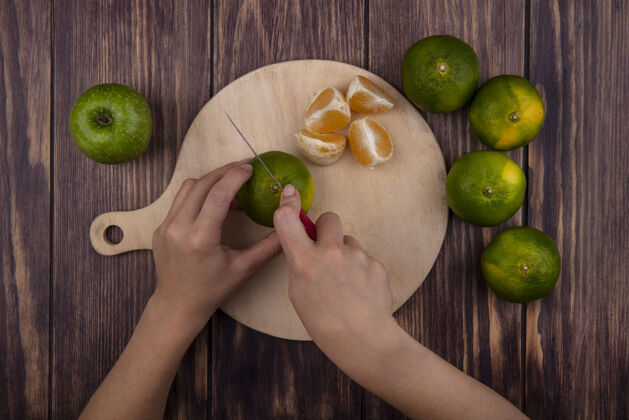 水果俯瞰图：一个女人在木墙上的砧板上切绿橘子橘子女人橘子