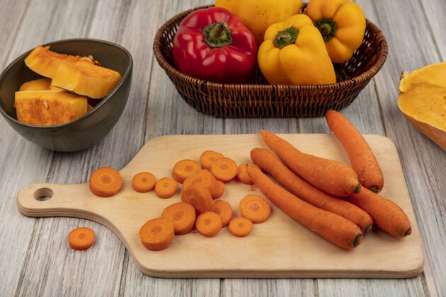 板顶视图健康的橙色胡萝卜上的木制厨房板上五颜六色的甜椒桶南瓜片在一个灰色的木制表面碗桶五颜六色健康