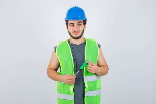 男性年轻的建筑工人穿着制服 手里拿着螺丝刀 一边望着别处 一边若有所思地看着前方成人专业工头