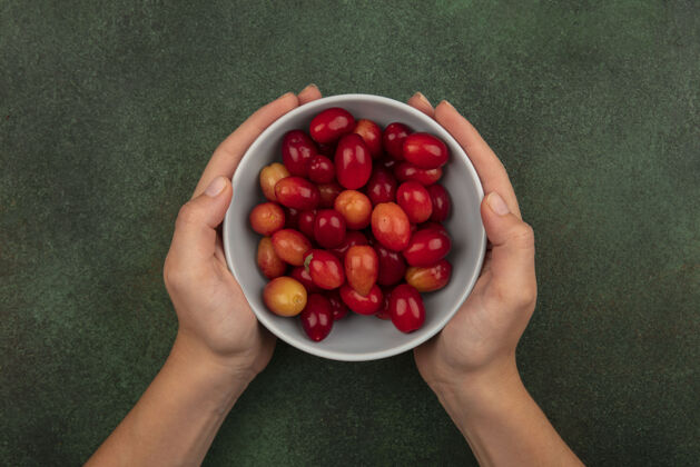 碗顶视图中的女性手拿着一碗新鲜的红凤梨樱桃在绿色的表面健康手营养