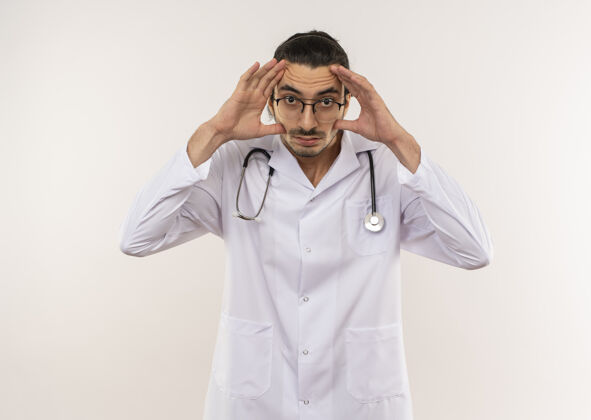 年轻年轻的男医生戴着眼镜 穿着白袍 手持听诊器 用手睁开眼睛男性光学男人