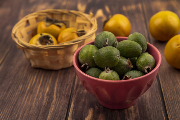 美味在木制表面的桶上放着柿子水果的碗上的美味新鲜的feijoas的俯视图饮食新鲜水果