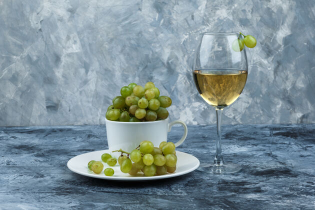 夏天一套葡萄酒和绿色葡萄在白色的杯子和盘子里 在肮脏的石膏背景上侧视图串路径壁板