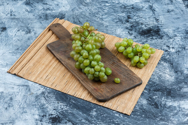 夏天在深蓝色大理石背景上 切菜板上的白葡萄和placemat高角度视图自然葡萄成熟