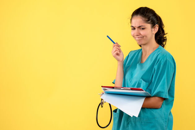 计算机前视图思考年轻女医生站在黄色背景上检查文件背景纸张年轻女医生