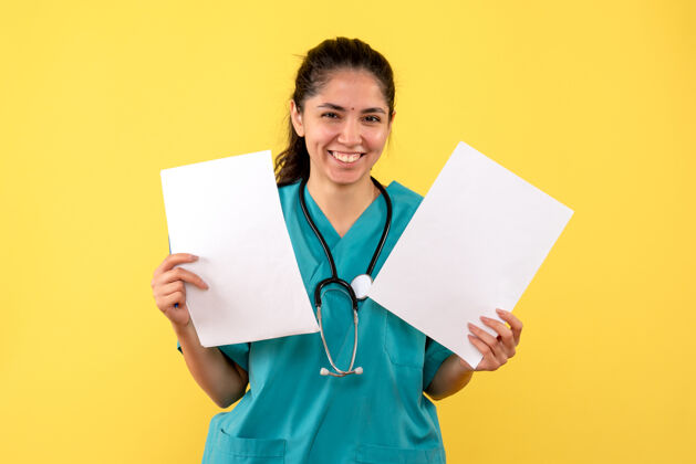 手正面图黄色背景上 穿着制服的女医生双手拿着纸大笑人员人员听诊器