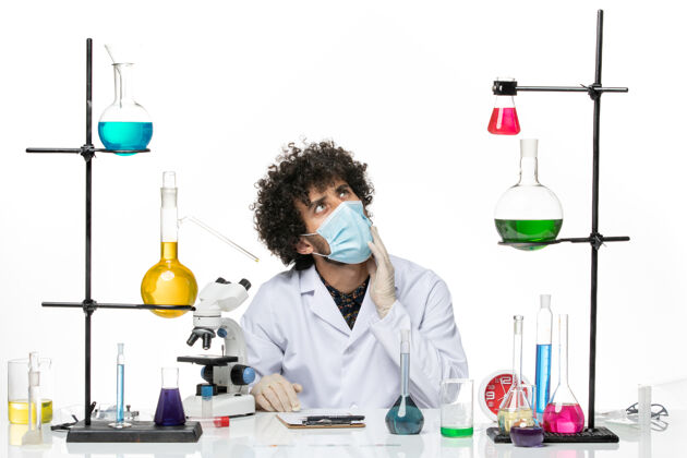 男性正面图男性化学家穿着医疗服 戴着口罩 坐在不同的解决方案上思考着白色空间解决方案医学男性化学家