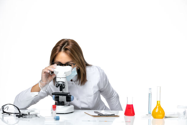 病毒前视图：女医生穿着白色医疗服 戴着口罩 在白色空间使用显微镜医学医学显微镜