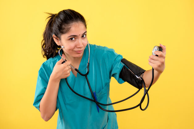 护士正面图：身着制服的女医生微笑着拿着黄色背景上的血压测量仪医疗器械医生血液