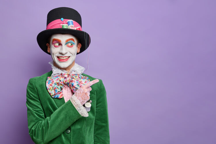 领结嘉年华派对上的笑脸男装有来自仙境的帽匠的形象 在空白处 穿着万圣节服装 在紫色的墙上隔离着明亮的妆容头发表演指标