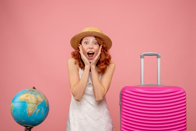 情感年轻女性游客的正面图 浅粉色的墙上挂着粉色的包夏天帽子模型