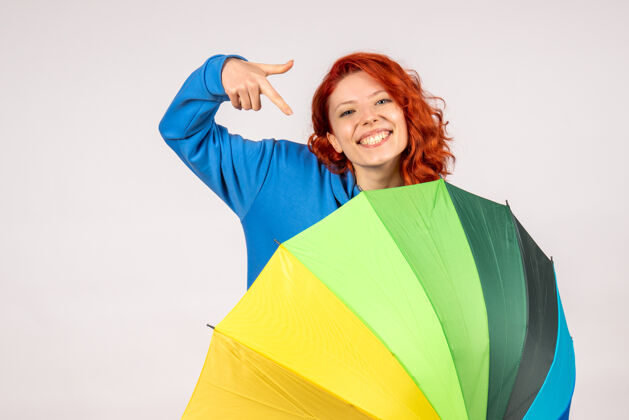 年轻的女性白色墙壁上带着彩色伞的年轻女性的正视图多彩前面快乐