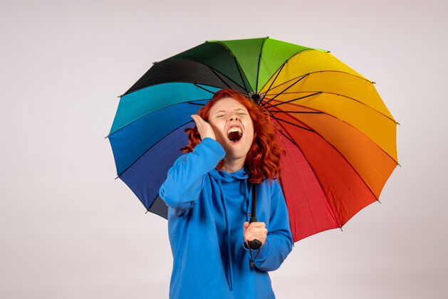 保护掩护白色墙壁上带着彩色雨伞的年轻女性的正视图女人天气彩虹