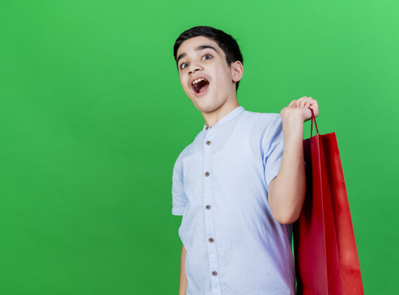 印象印象深刻的年轻白人男孩拿着购物袋隔离在绿色的墙壁与复制空间男孩男人购物