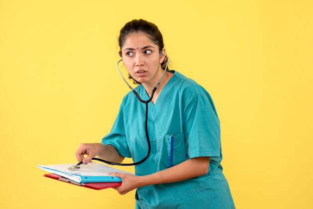 女医生穿着制服的女医生的正视图把听诊器放在黄色墙上的纸上成人听诊器肖像