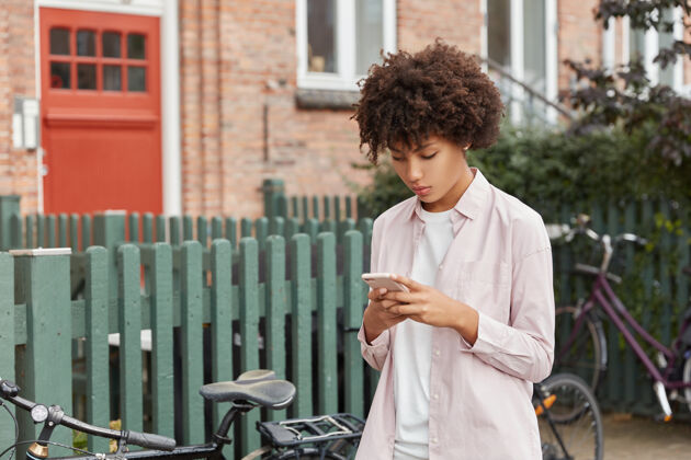 移动有着非洲发型的时髦博客在社交网络上看视频 在网站上看新闻 在围栏附近散步自行车应用程序自行车