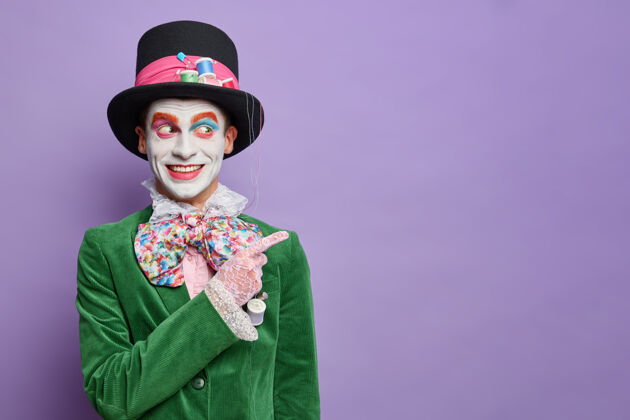 领结嘉年华派对上的笑脸男装有来自仙境的帽匠的形象 在空白处 穿着万圣节服装 在紫色的墙上隔离着明亮的妆容头发表演指标