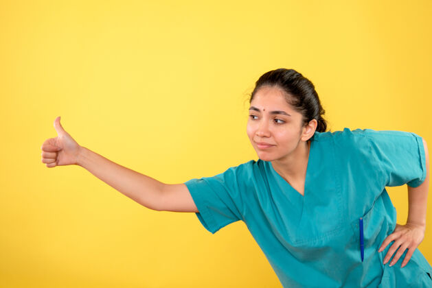 微笑黄色墙上年轻女医生竖起大拇指的正面图正面成人人