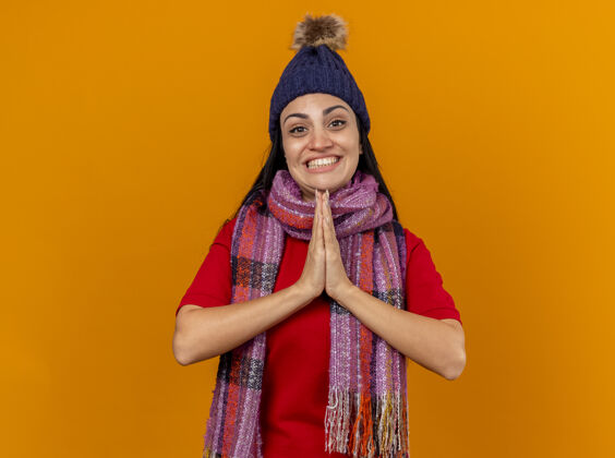 围巾微笑着的年轻白种人生病的女孩戴着冬天的帽子和围巾保持双手在橙色的墙上与复制空间隔离疾病年轻帽子