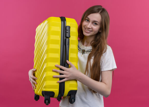 微笑微笑着的年轻旅行家女孩拿着手提箱在孤零零的粉红色墙上抱着女孩年轻人