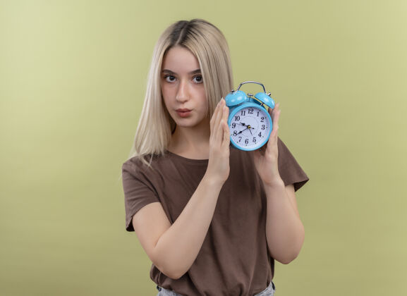 抱着年轻的金发女孩拿着闹钟看着隔离的绿色墙壁和复印空间闹钟时钟女人