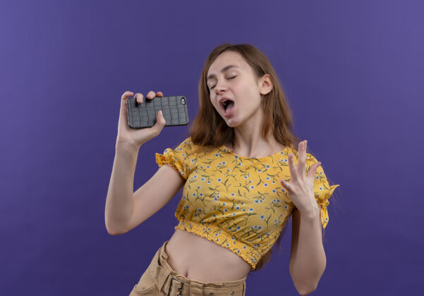 手机小女孩用手机当麦克风在孤零零的紫色墙上唱歌使用女孩年轻