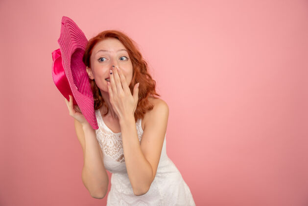 快乐粉红色墙上戴着粉红色帽子的年轻女性的正面图帽子年轻女性前面