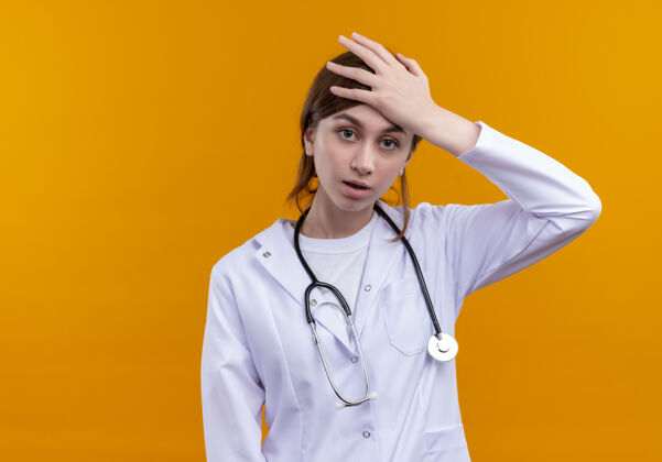 女人紧张的年轻女医生穿着医用长袍和听诊器把手放在头上孤立的橙色墙壁与复制空间听诊器医生女人