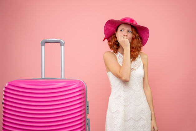 可爱年轻的女性游客与粉红色的帽子和袋子紧张的粉红色墙上的正面视图帽子快乐夏天