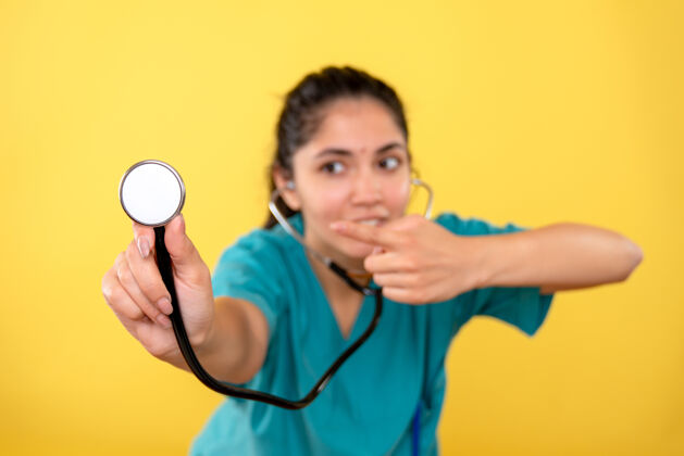 年轻女医生年轻女医生指着黄色墙上的听诊器的正视图医学微笑快乐