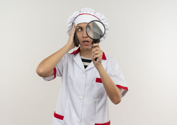 制服穿着厨师制服的年轻女厨师手持放大镜 手放在头上 看着白色的侧面 留有复印空间头手厨师