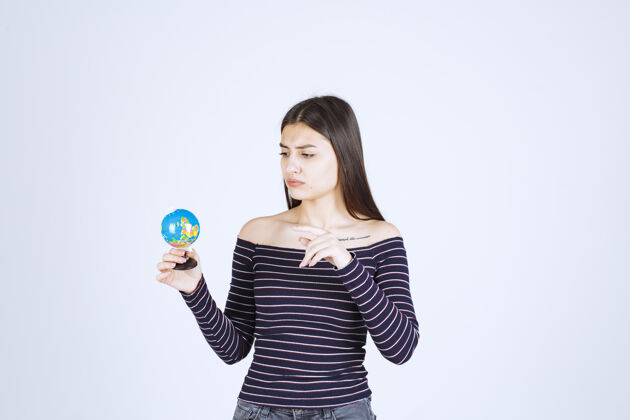 教育穿着条纹衬衫的年轻女子手里拿着一个迷你地球仪 在上面猜一个地方成人女性模型