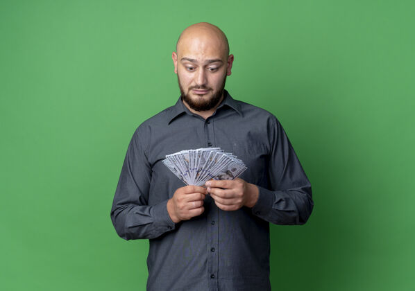 中心印象深刻的年轻秃头呼叫中心男子抱着钱 看着隔离在绿色与复制空间秃头印象金钱