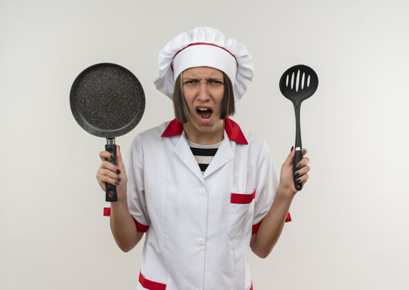抹刀愤怒的年轻女厨师穿着厨师制服 手里拿着抹刀和煎锅 看上去像是孤立的白色愤怒薯条年轻