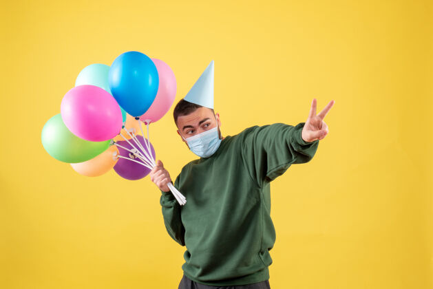 人正面图：年轻男性手持黄色背景上的彩色气球年病毒流行