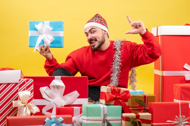 男人正面图：年轻男性围坐在礼物旁边 拿着黄色背景的礼物情感圣诞节年份