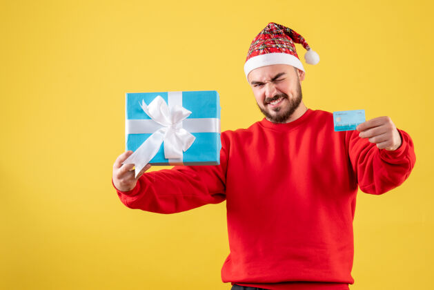 年轻男性正面图年轻男子手持圣诞礼物和黄色背景的银行卡男性微笑年份