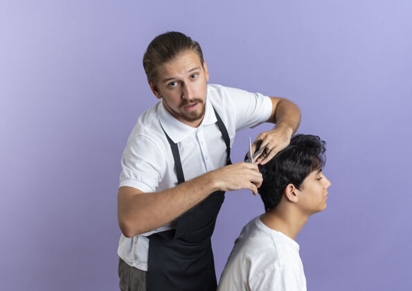 制服印象深刻的年轻帅哥理发师穿着制服做发型的年轻客户孤立的紫色与复制空间客户印象年轻