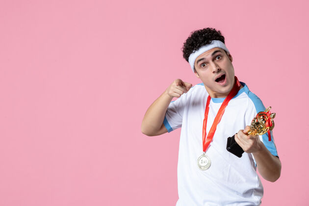 奖正面图：穿着运动服的年轻球员 在浅粉色的墙上戴着金杯和奖牌光体育奖牌