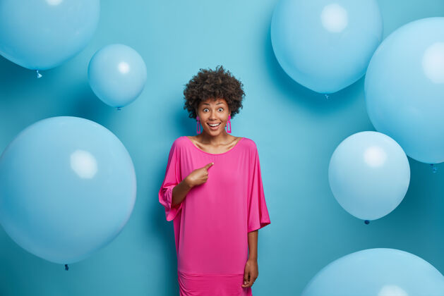 肖像照片中的惊喜开朗的女人指着自己 不敢相信成功 庆祝什么 穿着粉红色的裙子 站在气球周围生日气球微笑