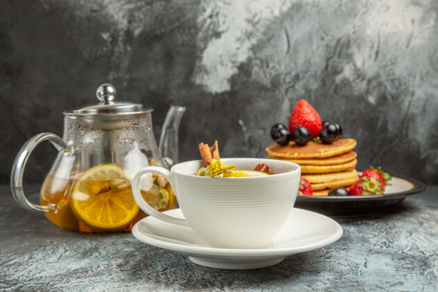 潘趣酒前视一杯茶 薄饼和水果放在黑暗的表面上早餐食物茶碟茶瓷器