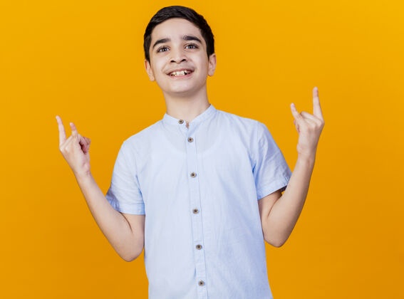 年轻微笑着的年轻白人男孩看着摄像机做着橙色背景上孤立的摇滚标志微笑摇滚橙色