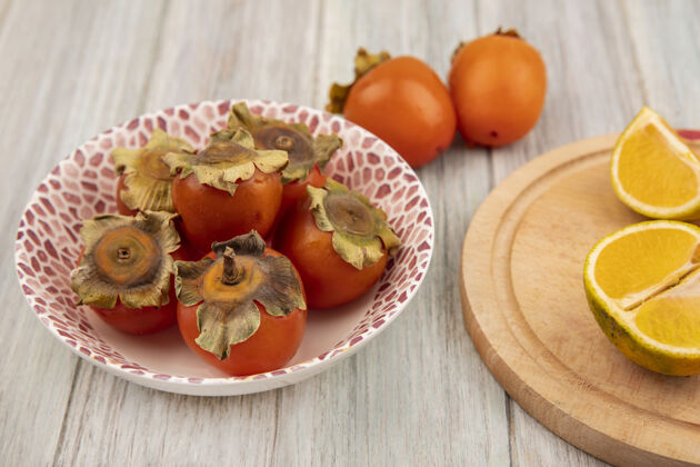 柿子新鲜柿子放在碗上的顶视图 橘子放在灰色木墙上的木制厨房板上秋天板子木头