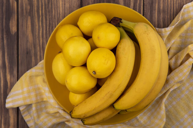 盘子顶视图富含维生素的柠檬放在黄色格子布上的黄色盘子上 香蕉放在木墙上木头新鲜水果