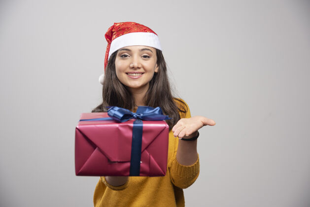 模型戴着圣诞帽的微笑女人展示着一个礼品盒黑发帽子肖像